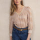 Woman wearing a striped shirt and blue jeans against a beige wall